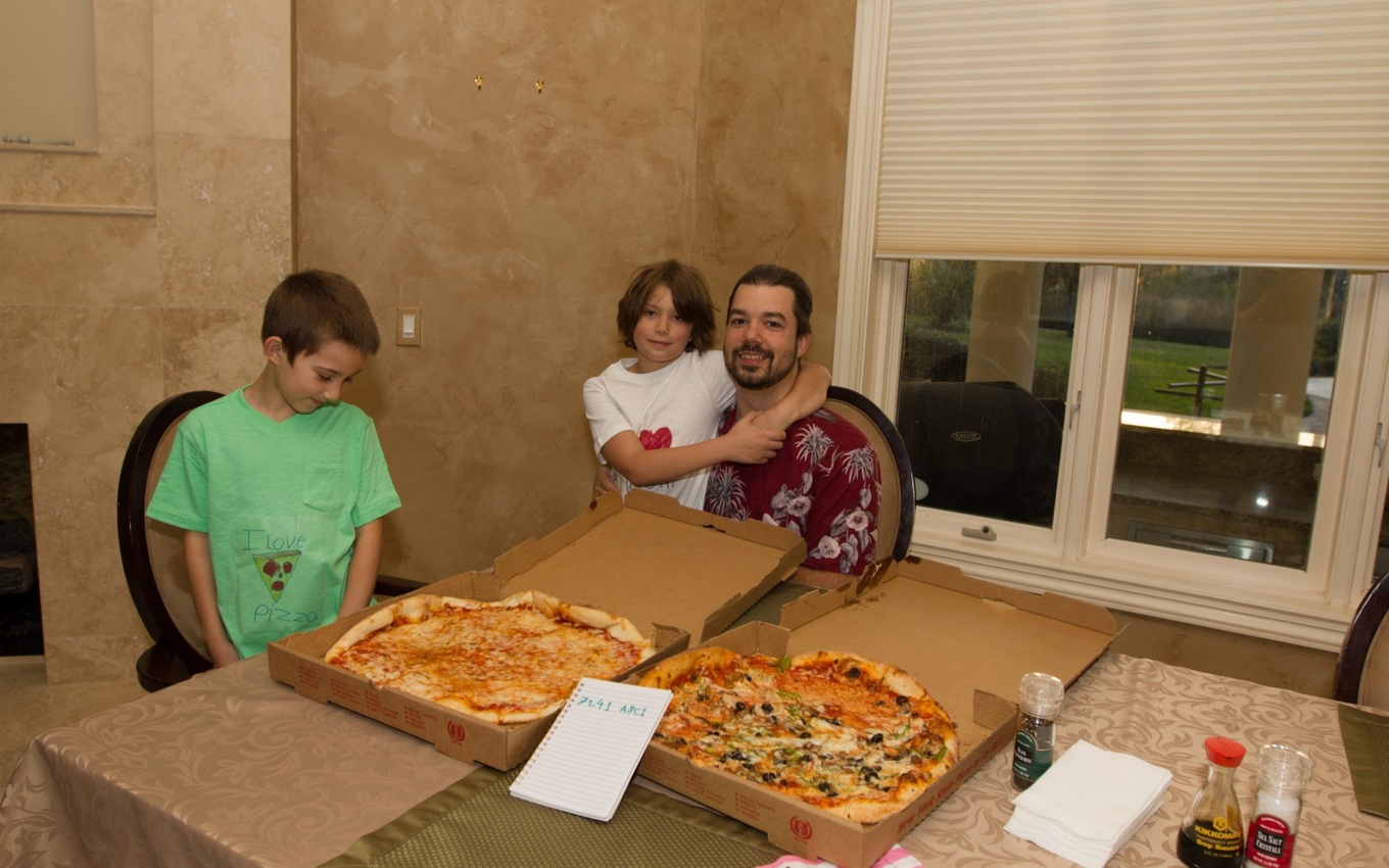 A family enjoying pizza with two large pizzas on the table